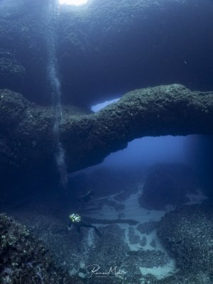 der Double Arch in Gozo in der Xwejni Bay. Ein Taucher erkundet die beeindruckende Unterwasserlandschaft währen das Sonnenlicht von oben mystisch die Szenerie beleuchtet