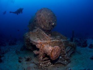 Eine Lokomotive liegt auf dem Meeresboden, die von Meeresorganismen bewachsen und mit einer Patina überzogen ist. Die Lokomotive wurde bei der Explosion auf der SS Thistlegorm nach dem Bombentreffer von Deck geschleudert. Im blauen Wasser schwebt ein Taucher, der die majestätische Szene erkundet und die friedliche Atmosphäre dieser versunkenen Lokomotive einfängt.