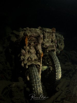 Ein mit Sediment und Bewuchs bedecktes Motorrad im Inneren des Wracks der SS Thistlegorm. Zwischen den Rädern hat sich ein kleiner Fisch versteckt. Ein faszinierendes Zeugnis der Unterwasser-Zeitkapsel.