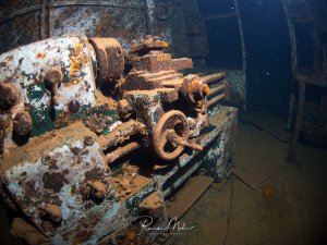 Eine stark korrodierter Werkbank steht im Inneren eines Wracks auf dem Meeresgrund. Die Metallteile sind vollständig von Rost überzogen und zeigen die fortgeschrittene Zersetzung nach jahrelanger Unterwasserexposition.